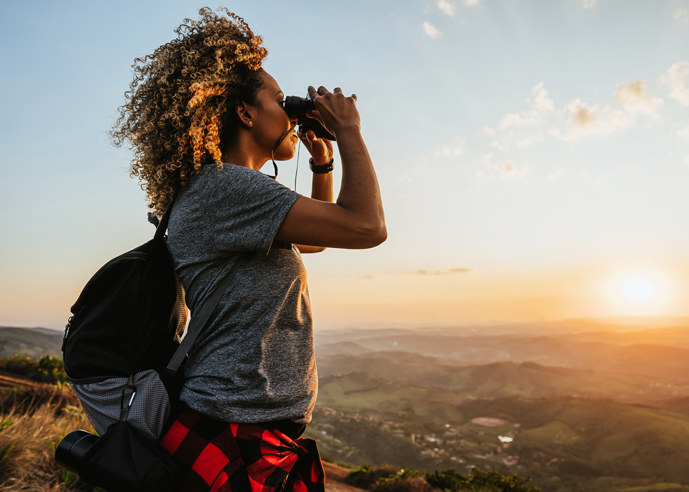 Woman looking through binoculars at a beautiful sunrise