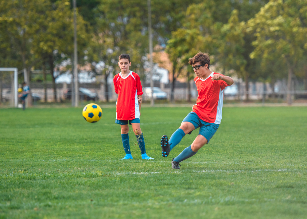 Child wearing sports glasses while kicking a soccer ball