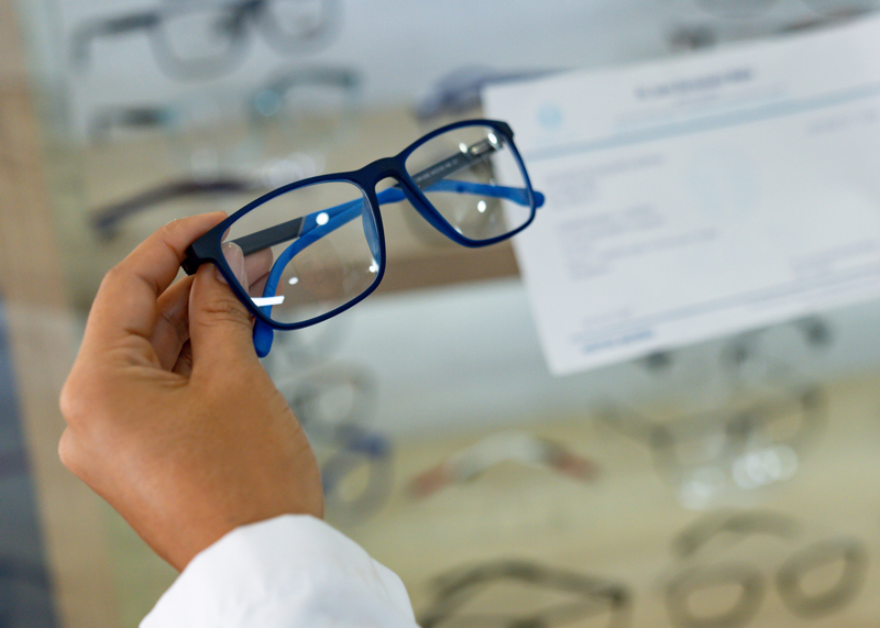 Hand holding a pair of eyeglasses over a prescription